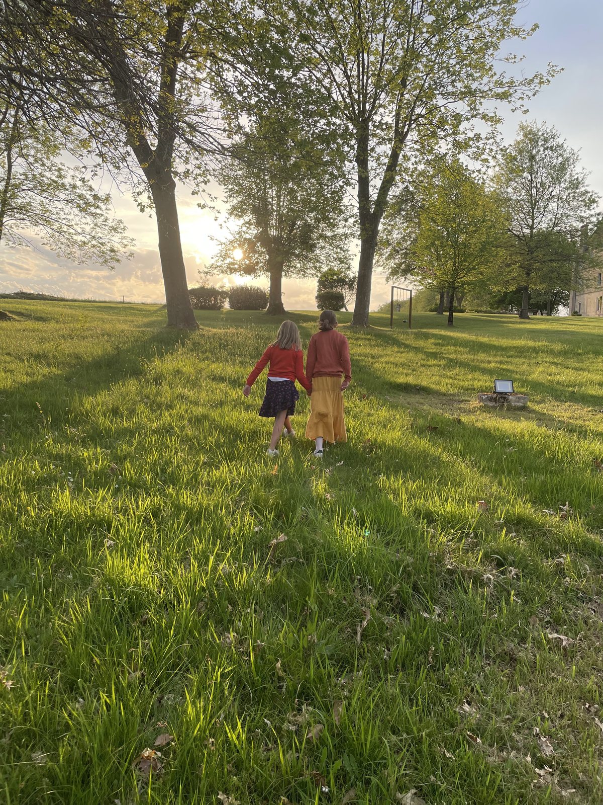 Deux enfants marchant main dans la main vers le soleil couchant, sous les grands arbres