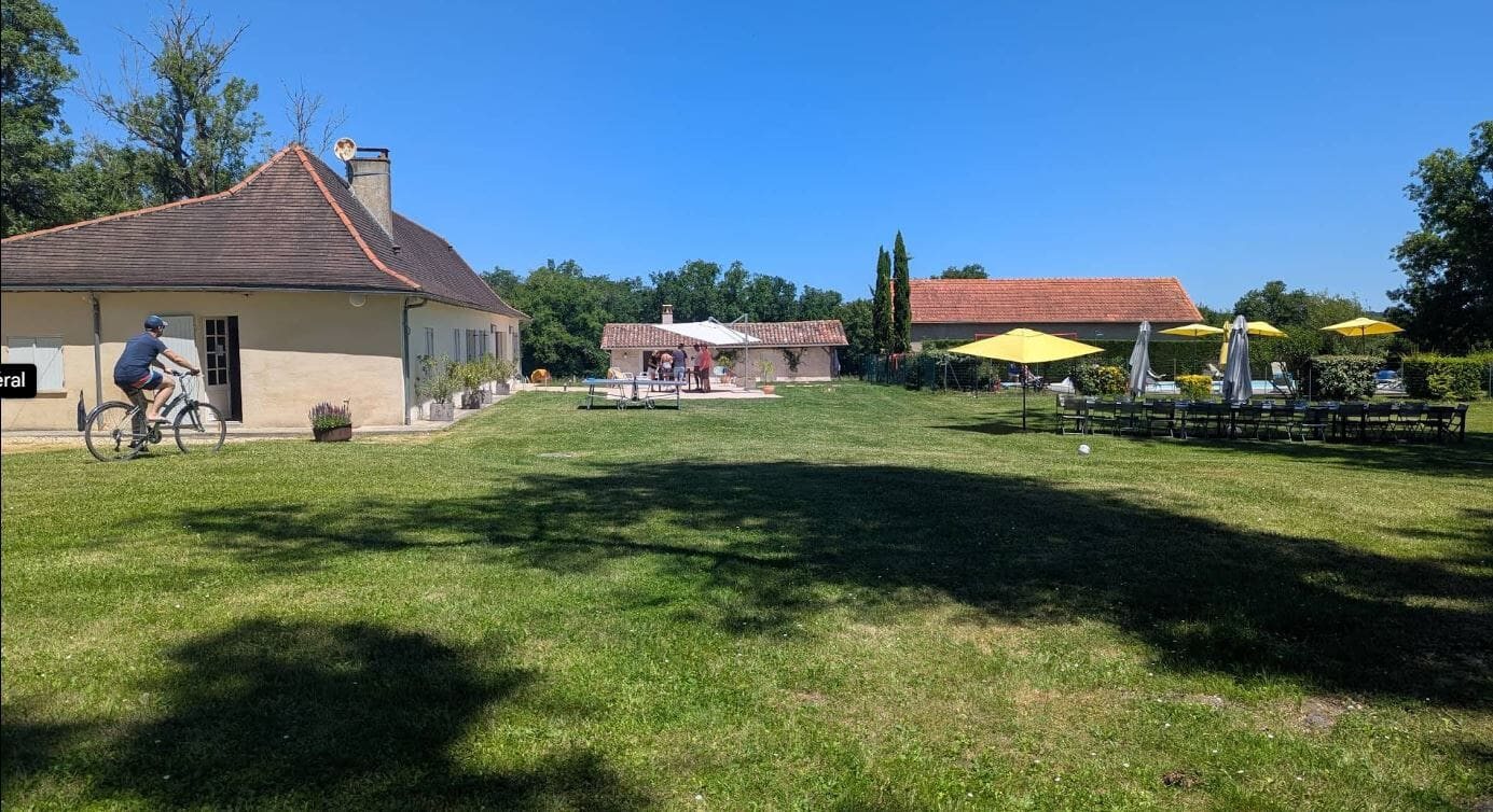 La grande pelouse devant La Longère : vélo, parasols jaunes et piscine au fond